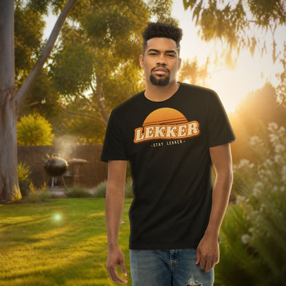 Stay Lekker Tee – black tee with retro sunset 'LEKKER' print in a backyard at golden hour with a braai
