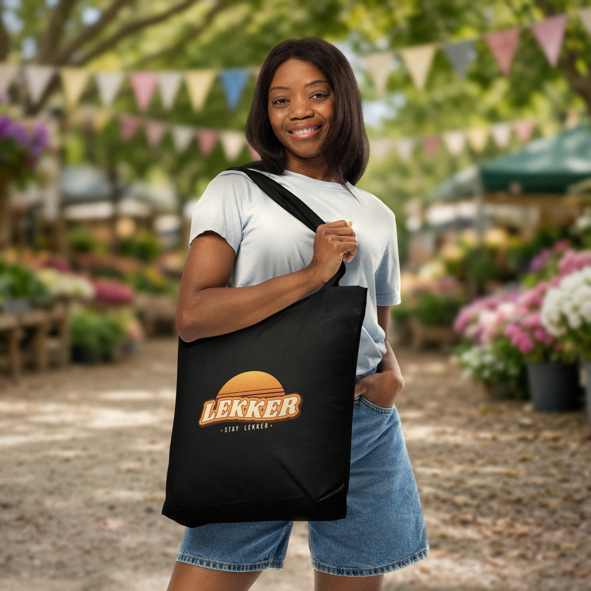 Stay Lekker Tote Bag in black with retro sunset 'LEKKER – stay lekker' print, carried at a sunny farmers market