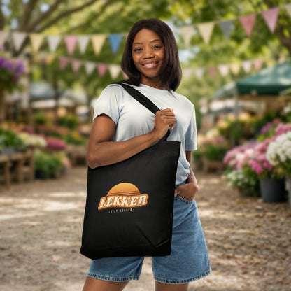 Stay Lekker Tote Bag in black with retro sunset 'LEKKER – stay lekker' print, carried at a sunny farmers market