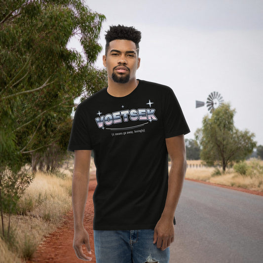 Voetsek Tee in black – man wearing the Afrikaans 'Voetsek' print t-shirt on a country road with a windmill