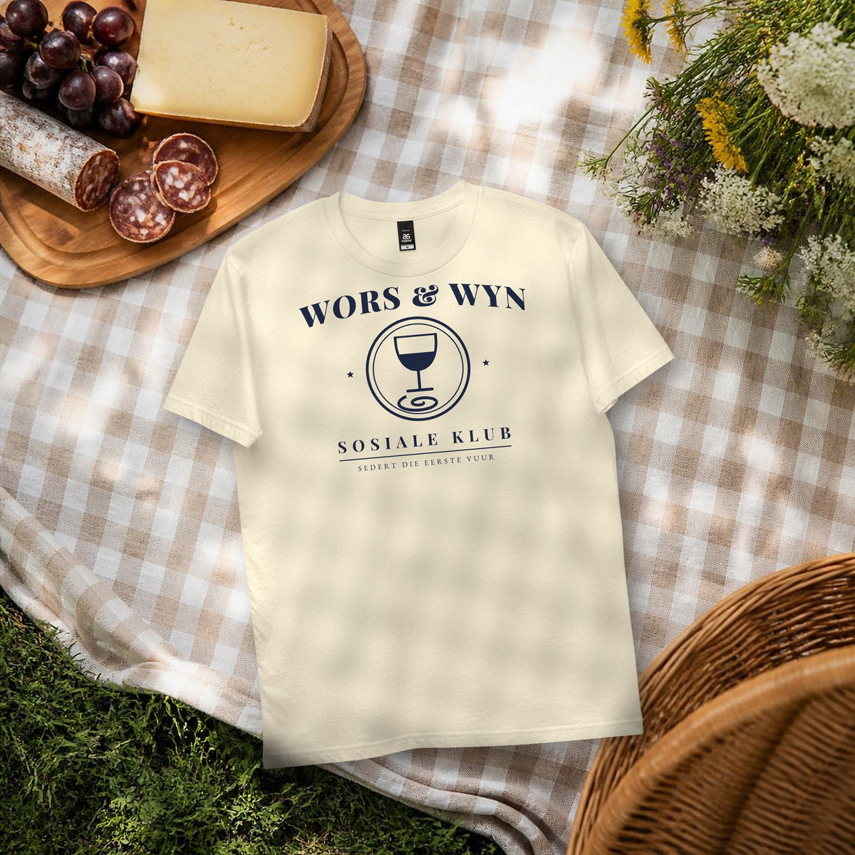 Wors & Wyn Sosiale Klub Tee in natural – flat lay on a picnic blanket with cheese, grapes and droë wors