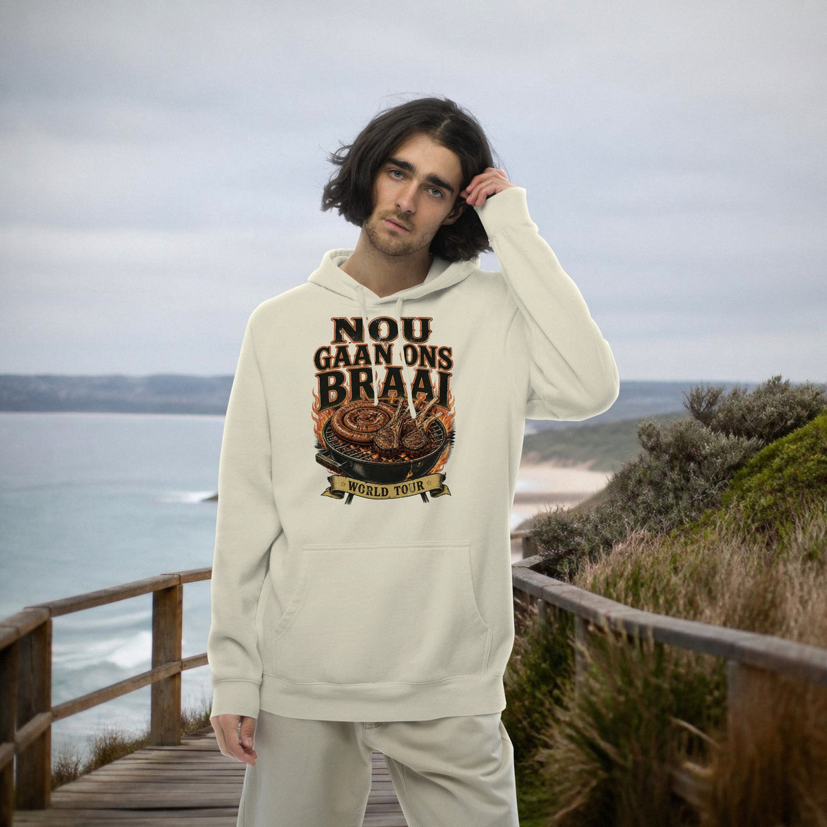 Nou Gaan Ons Braai Hoodie – man wearing the 'Nou Gaan Ons Braai World Tour' braai print hoodie on a coastal boardwalk