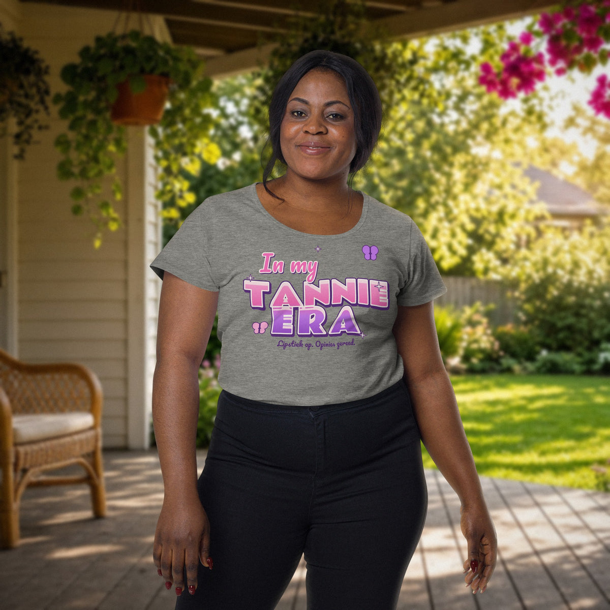 In My Tannie Era women's tee in grey marle – woman wearing the pink and purple 'In my Tannie Era' print on a sunny stoep with garden